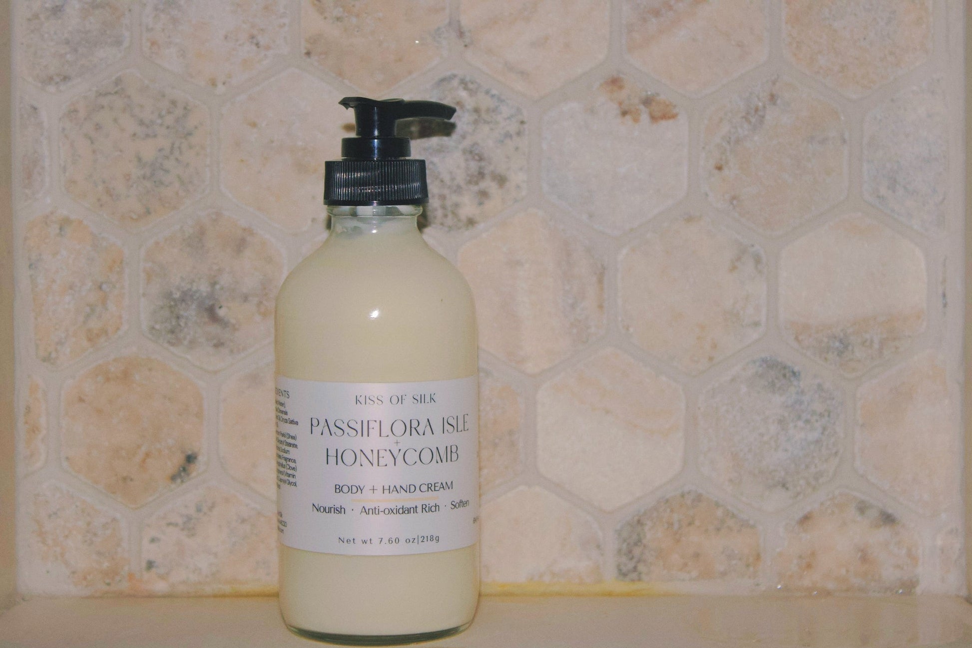 A bottle of Kind of Sea Passiflora Isle Honeycomb body and hand cream, featuring a black pump and white label, set against a beige hexagonal tile background.